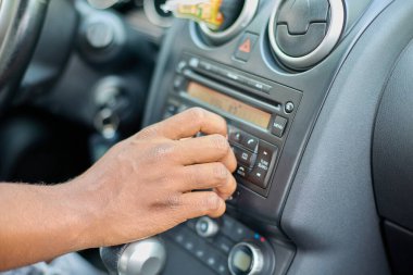 Siyah bir adamın eli, arabanın stereo sisteminin sesini ayarlar..