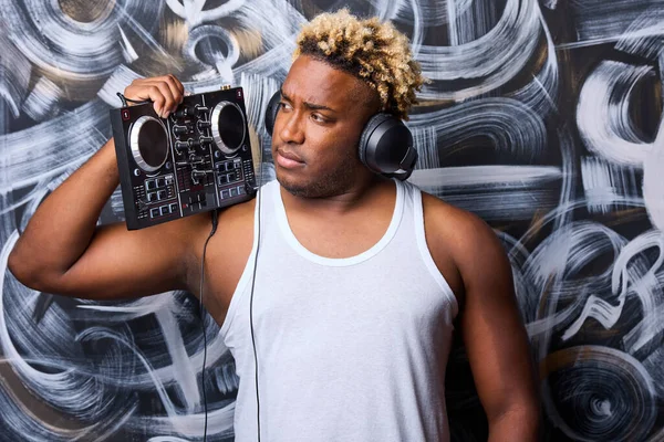 Un DJ afroamericano con una consola de DJ en un club contra una pared con graffiti — Foto de Stock