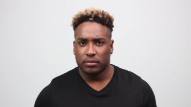Ciddi bir Afrikalı adam kamerayı işaret eder ve sonra parmağını dudaklarına koyar.