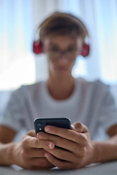 Σύγχρονη έφηβος με ακουστικά και ένα λευκό T-shirt κοιτάζει το τηλέφωνο. — Φωτογραφία Αρχείου