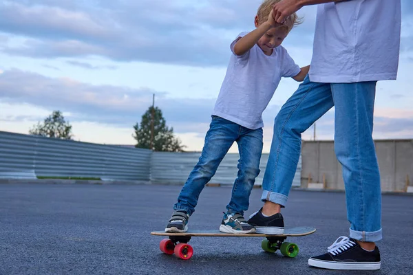 Boy enseña a un niño a montar un monopatín, le ayuda a subirse a un monopatín. — Foto de Stock