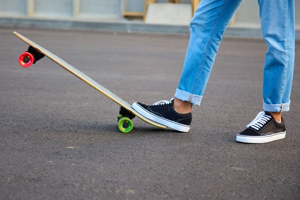 Adolescente em jeans azuis faz truques em um skate infantil. — Fotografia de Stock