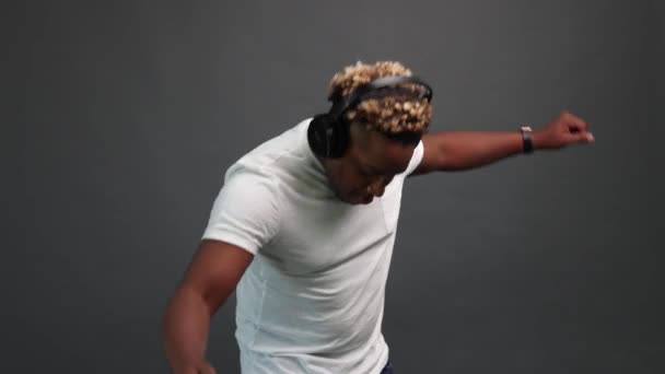 Bailando de un hombre negro sobre un fondo gris con auriculares — Vídeos de Stock