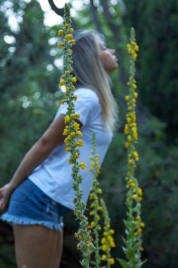 Güzel bir kadının dikey fotoğrafı sarı çiçeklerin kokusundan keyif alıyor.