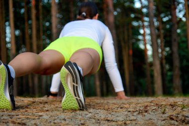 Genç atletik kadın ormanın arka planında şınav çekiyor..