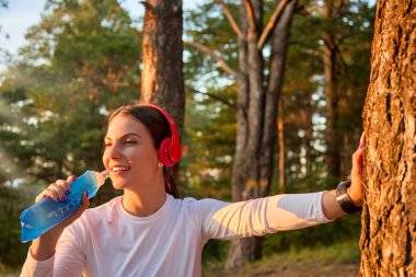 Kulaklıklı neşeli sporcu antrenmandan sonra tekrar kullanılabilir yumuşak bir spor şişesinden su içiyor.