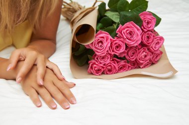 Bir kadın güzel bir buket pembe gülle bir yatakta yatıyor..