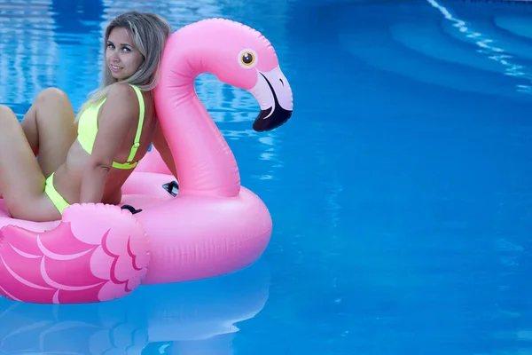 Vrouw zwemt in het zwembad van het hotel vast te houden aan een opblaasbare roze flamingo. — Stockfoto