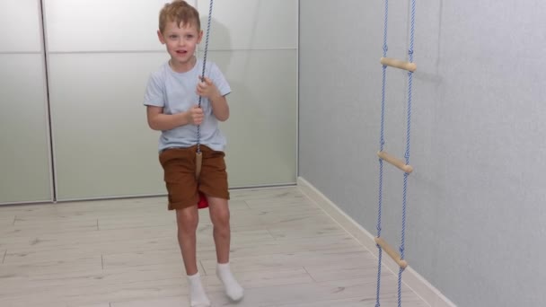 Cute happy little boy swinging on a rope swing at home — Wideo stockowe