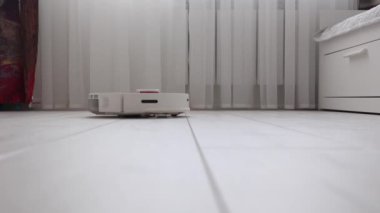 White robot vacuum cleaner effectively cleans the light laminate in the room