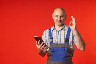 Man in a protective jumpsuit holds a digital tablet and shows the OK sign