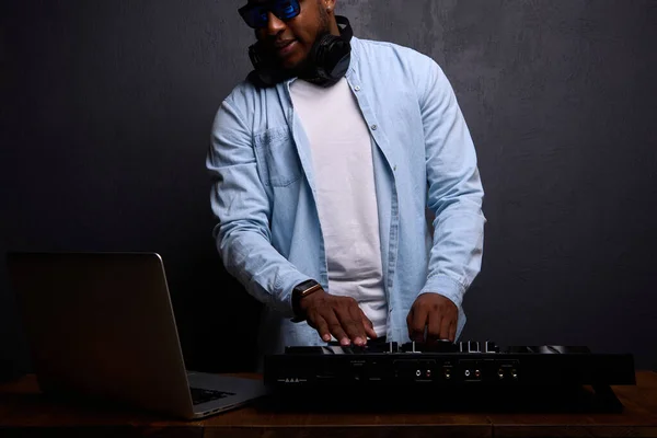 DJ afroamericano con auriculares y gafas de sol funciona en un estudio. — Foto de Stock