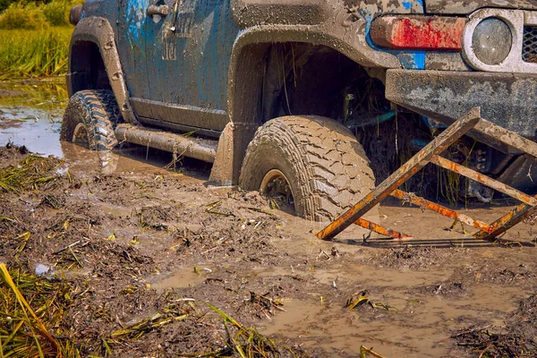 Off-road αυτοκίνητο έχει κολλήσει σε μια λακκούβα της λάσπης και προσπαθεί να φύγει χρησιμοποιώντας μια ράμπα. — Φωτογραφία Αρχείου