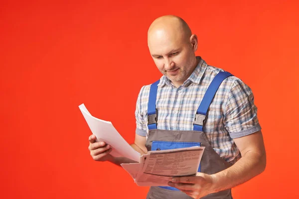 Glatzköpfiger Mann in Arbeitskleidung hält Unterlagen in den Händen — Stockfoto