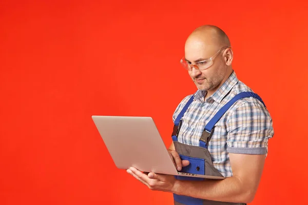 Skallig man i arbetskläder arbetar på en bärbar dator som håller den i sina armar — Stockfoto