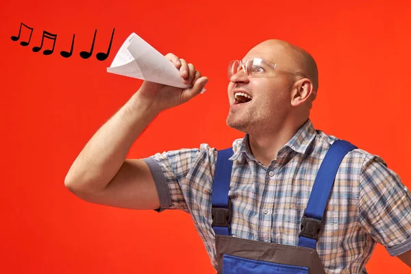 Bald man in work clothes sings into a rolled-up pipe made of paper — Stock Photo, Image