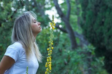 Beyazlar içindeki güzel kadın sarı bir narin çiçeği kokluyor..