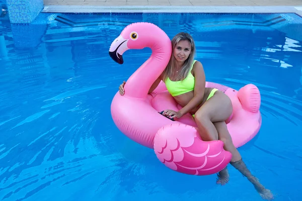 Vrouw zwemt in het zwembad knuffelen een opblaasbare roze flamingo speelgoed. — Stockfoto