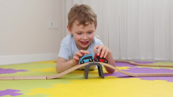 Улыбающийся мальчик веселится, играя с деревянными игрушками на ковриках-головоломках — стоковое видео