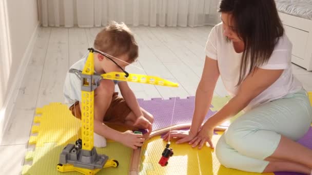 Мама и сын веселятся, играя на игрушечной железной дороге и игрушечном кране в детской. — стоковое видео