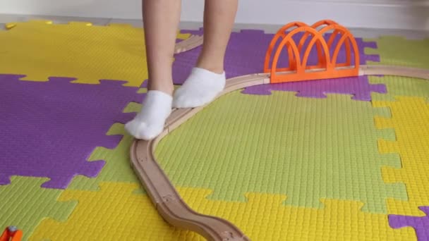 Bambino in calzini bianchi cammina lungo una ferrovia di legno giocattolo, bilanciamento — Video Stock