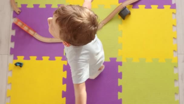Caucasico ragazzo biondo allarga le braccia ai lati e gira sui tappetini puzzle — Video Stock
