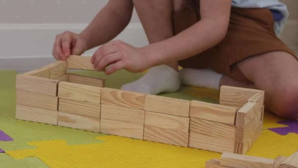Închiderea unui copil care construiește un perete de bare de lemn pe covoare de puzzle. — Videoclip de stoc