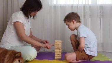 Oğlan ve annesi jenga oynuyorlar, kırmızı bir köpek yakınlarda dinleniyor.. 