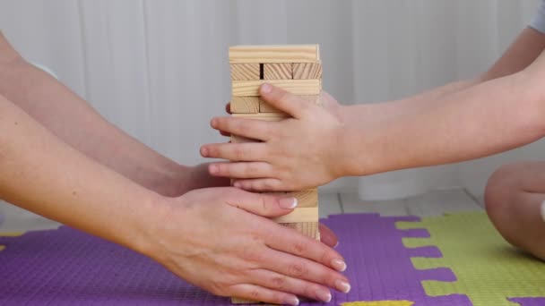 Mamá y su hijo juntos instalan una torre de barras de madera en alfombras de rompecabezas — Vídeo de stock