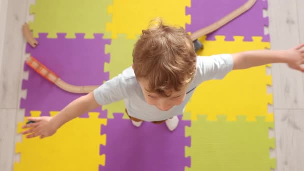 Caucasico ragazzo biondo allarga le braccia ai lati e gira sui tappetini puzzle — Video Stock