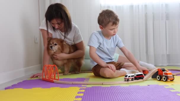 Мама и сын проводят время вместе, играя в игрушечную железную дорогу в детской на ковриках-головоломках — стоковое видео