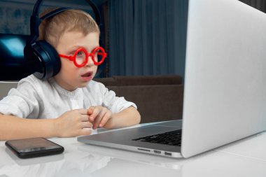 Kırmızı gözlüklü küçük bir çocuk evde online eğitim kursu alıyor.