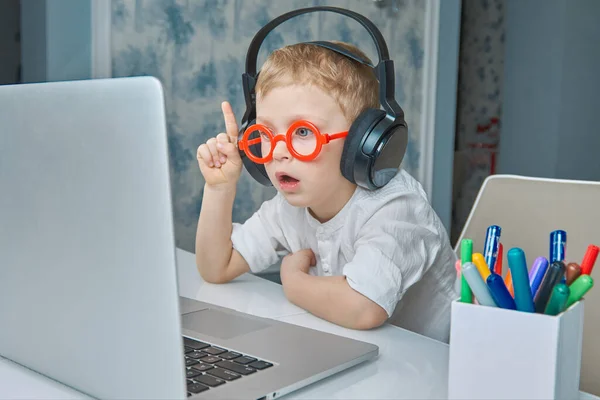 Ένα παιδί με κόκκινα γυαλιά και ακουστικά διασκεδάζει επικοινωνώντας μέσω video link χρησιμοποιώντας ένα laptop. — Φωτογραφία Αρχείου