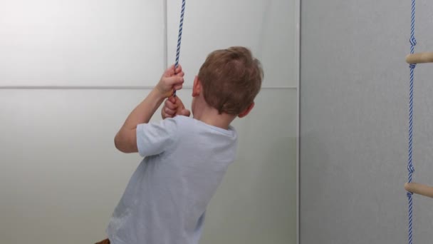 Cute happy little boy swinging on a rope swing at home — 图库视频影像