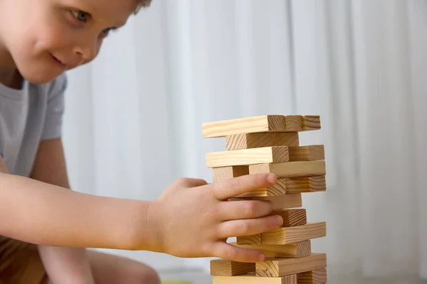 Criança branca bonito diligentemente desmonta uma torre feita de barras de madeira. — Fotografia de Stock