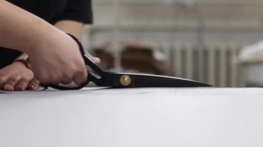 Terzi, dikiş atölyesinde makasla kumaş kesiyor.