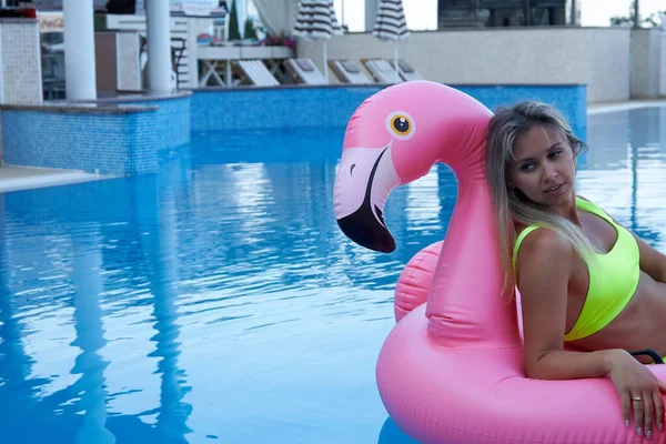 Mooie vrouw zwemt op een roze opblaasbare flamingo in het hotel zwembad. — Stockfoto
