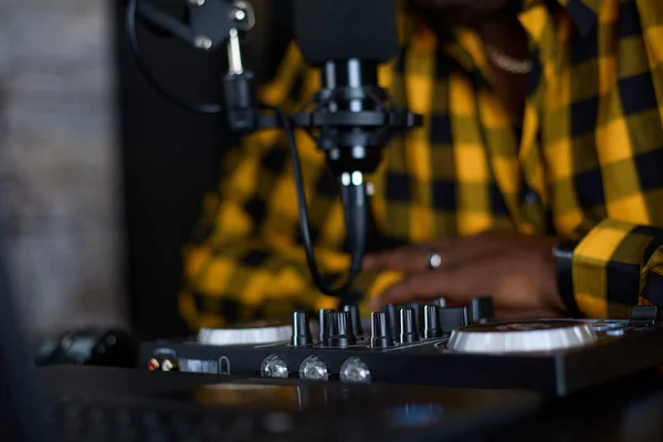 Small studio with studio equipment for close-up music production. A record player, a mixer, a laptop and a microphone against the background of a blurry black man in a bright plaid shirt