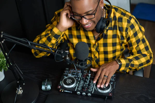 Top view of a musician creating music in his home studio, mixing on a DJ console. An African man using a remote control, laptop, headphones and microphone records music tracks