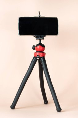 Kırmızı ve siyah bir masaüstü telefon tripodu pembe arka planda duruyor. Fotoğraf ve mesaj için yer var. Tripod ve telefon.