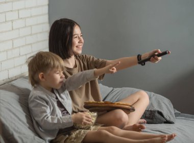 Bir erkek ve bir kız kanepede oturuyor, televizyonu gösteriyor ve gülüyor, ev yapımı pizza ve patlamış mısır yiyorlar. komedi kavramı