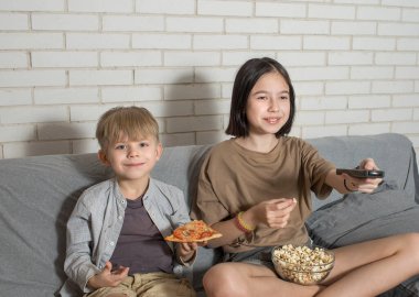 Bir erkek ve bir kız kanepede oturmuş televizyon izliyor, ev yapımı pizza ve patlamış mısır yiyorlar. Kardeş iletişimi kavramı.