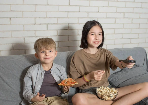 Bir erkek ve bir kız kanepede oturmuş televizyon izliyor, ev yapımı pizza ve patlamış mısır yiyorlar. Kardeş iletişimi kavramı.