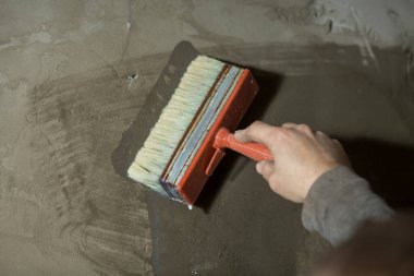 Adamın eli yakın planda, beton duvarı eski bir fırçayla kaplıyor.