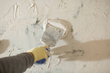 Duvara yakın bir spatulayla alçı havan macunu sürme işlemi.