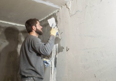 Sakallı bir erkek alçı beton bir duvarı spatulayla kaplıyor.