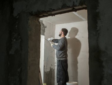 Sakallı bir erkek alçı beton bir duvarı spatulayla kaplıyor.