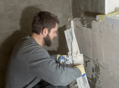 Sakallı bir adam pencere pervazının altına bir spatula yapıştırıyor..