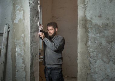 Alçıcı sakallı bir adam odanın köşesinde delinmiş bir resim köşesine asıyor, elinde bir spatul.