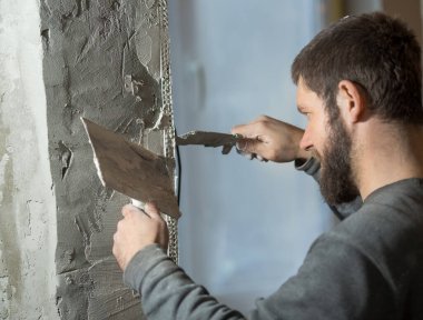 Alçıcı sakallı bir adam odanın köşesinde delinmiş bir resim köşesine asıyor, elinde bir spatul.